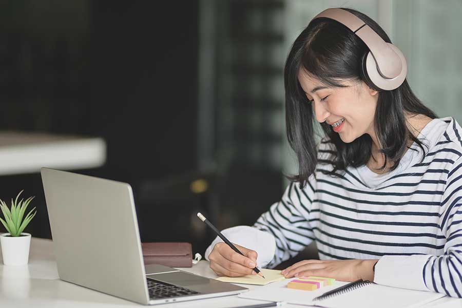 Femme asiatique écrivant sur le bloc-notes avec un ordinateur portable et des écouteurs.