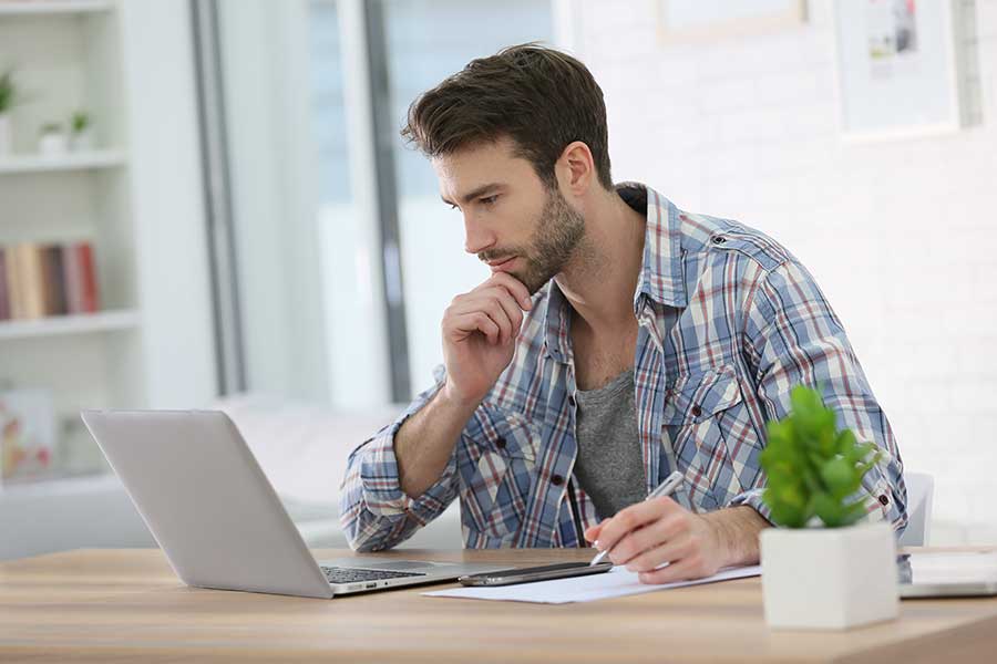 Young man writing copy on notapad while looking at laptop. 