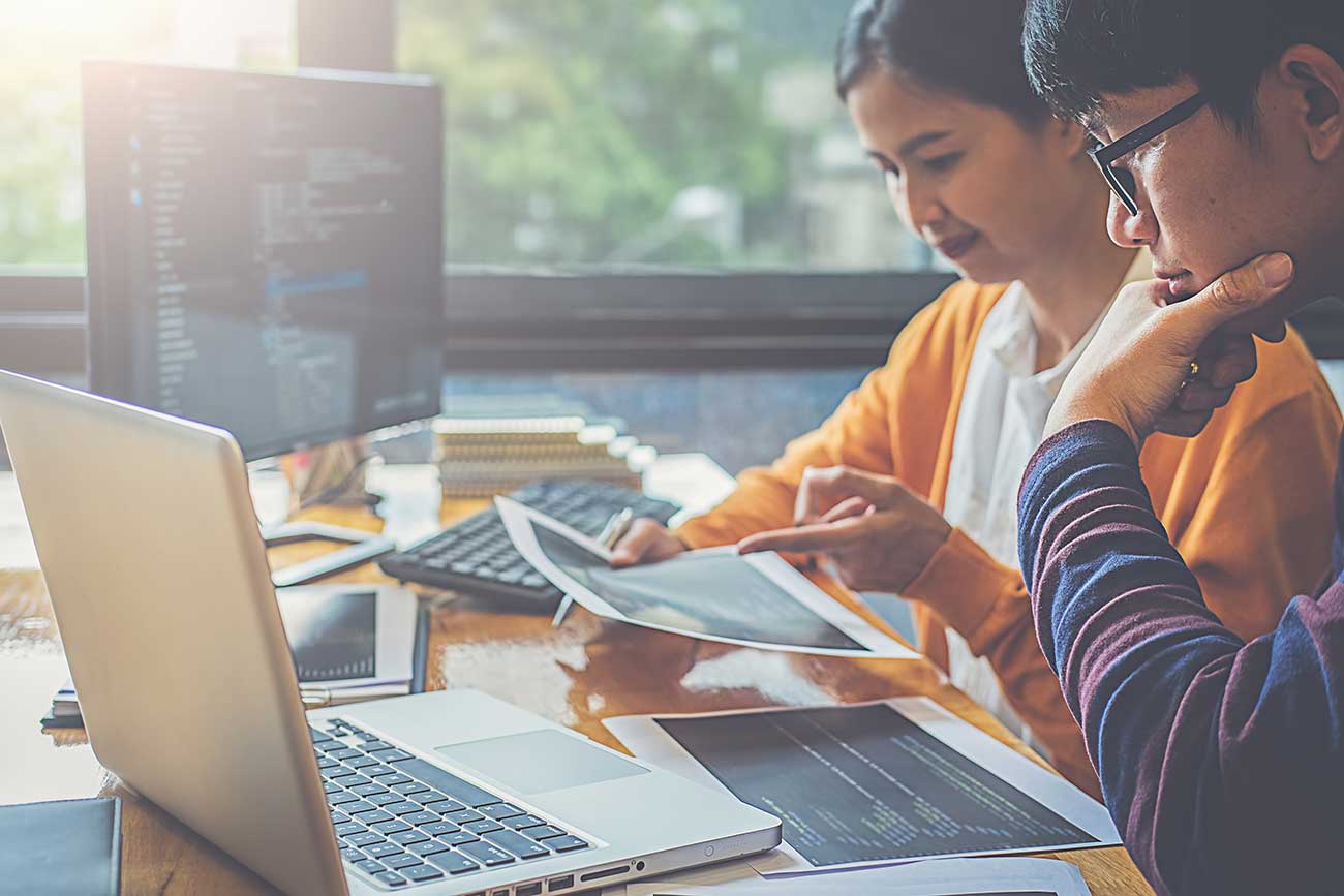 Two people looking at paperwork in front of a computer