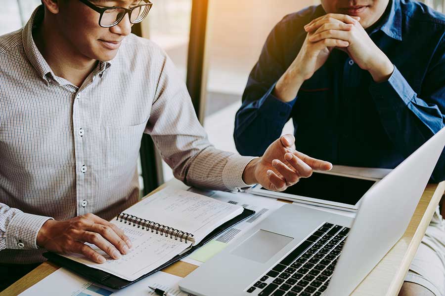 Deux hommes sur un ordinateur portable avec un bloc-notes de travail