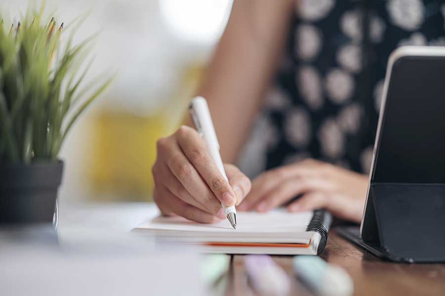 Woman's hand writing on a notepad beside laptop