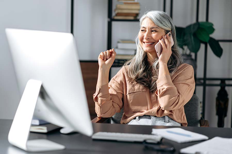 Femme d’âge moyen sur le téléphone cellulaire au bureau de l’ordinateur