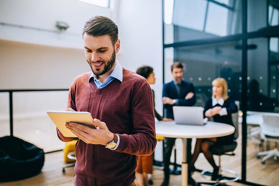 Homme sur iPad avec une équipe de personnes derrière lui sur un bureau dans les bureaux 