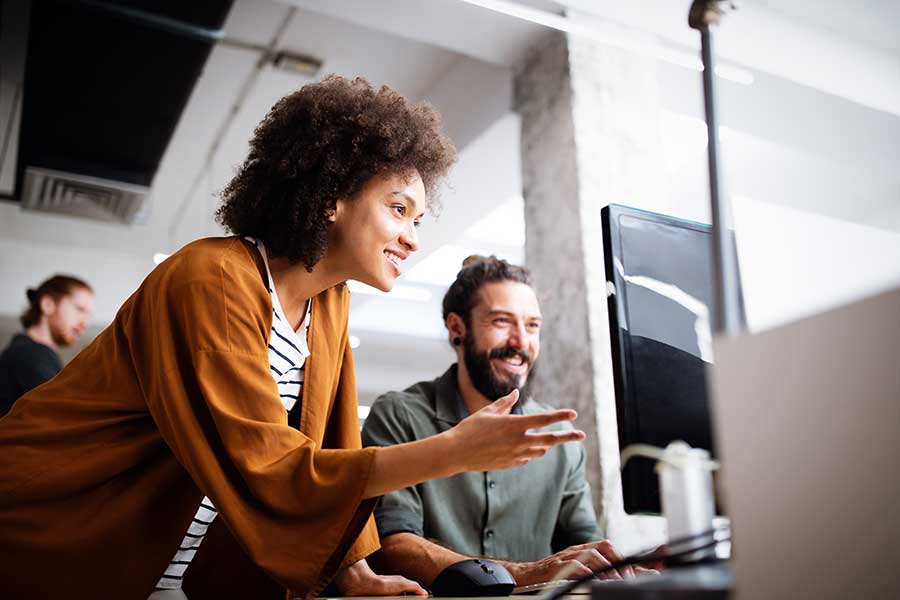 L’homme et les femmes bureau bureau regardant l’écran d’ordinateur. Les deux sourient et elle pointe vers l’écran.