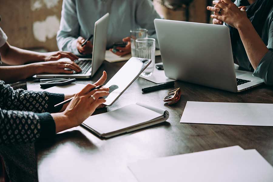 Group of people around a computer desk with documents and devices. Only hands in shot.