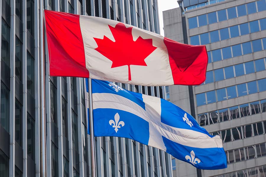 Drapeau québécois et canadien agitant à l’extérieur d’un immeuble de grande hauteur