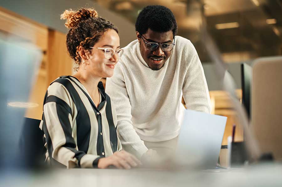 Un homme et une femme travaillant à un ordinateur sur un bureau discutant d’un projet. 