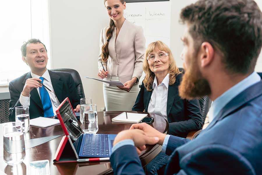 Two men and two women at a meeting smiling. One woman standing with a printed sheet.