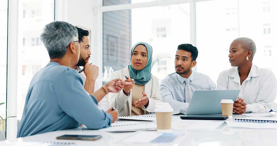 Five people at a desk conversing.